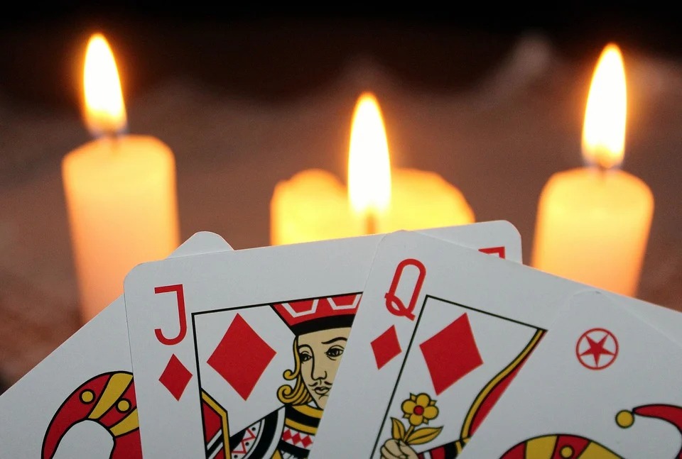 Karty: dwa czerwone jokery, walet i dama karo na tle płonących trzech świeczek. 