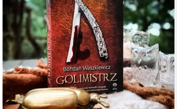 na zdjęciu znajduje się książka Golimistrz przed nią złota figurka żuka a wokół szklane figurki sówek