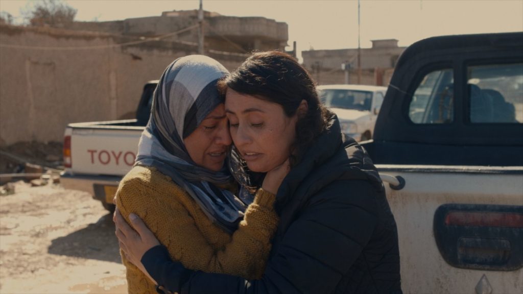 kadr z filmu "Anioły z Sindżaru"-  główna bohaterka Hanifa przytulona  z siostrą na tle samochodów 