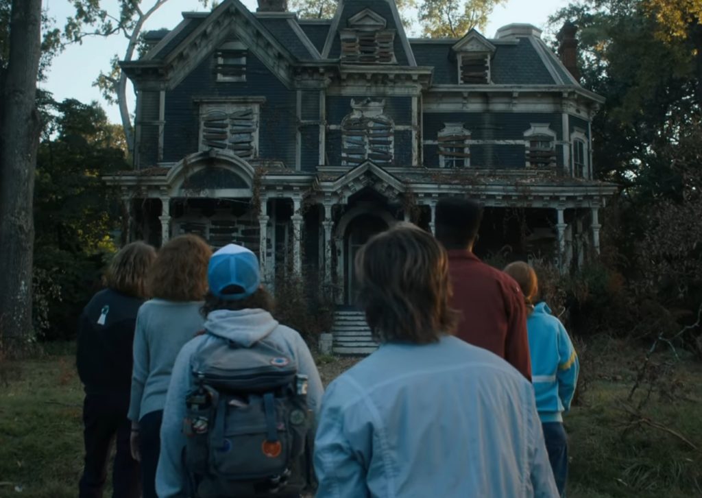 bohaterzy serialu stranger things odwróceni tyłem do kamery, a przed nimi stoi przerażający stary dom.