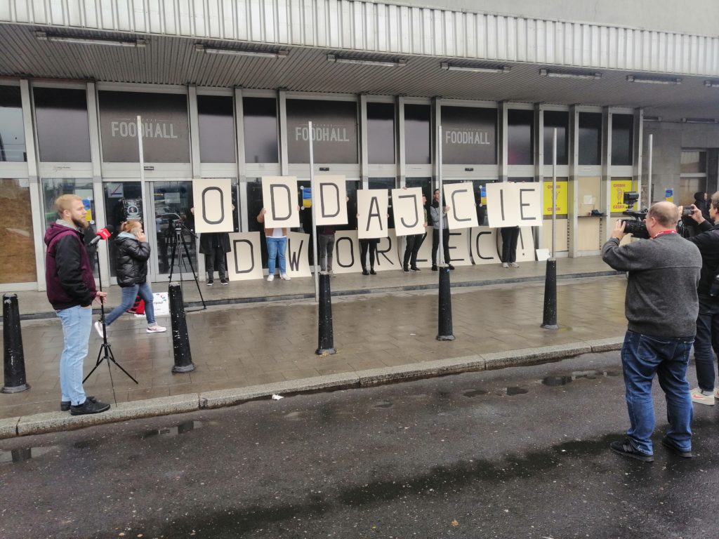 Protestujący przed budynkiem dworca głównego, trzymający kartony z napisem "oddajcie dworzec".