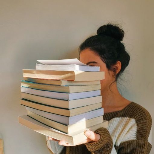 Kobieta zasłonięta przez stos książek, który trzyma w rękach